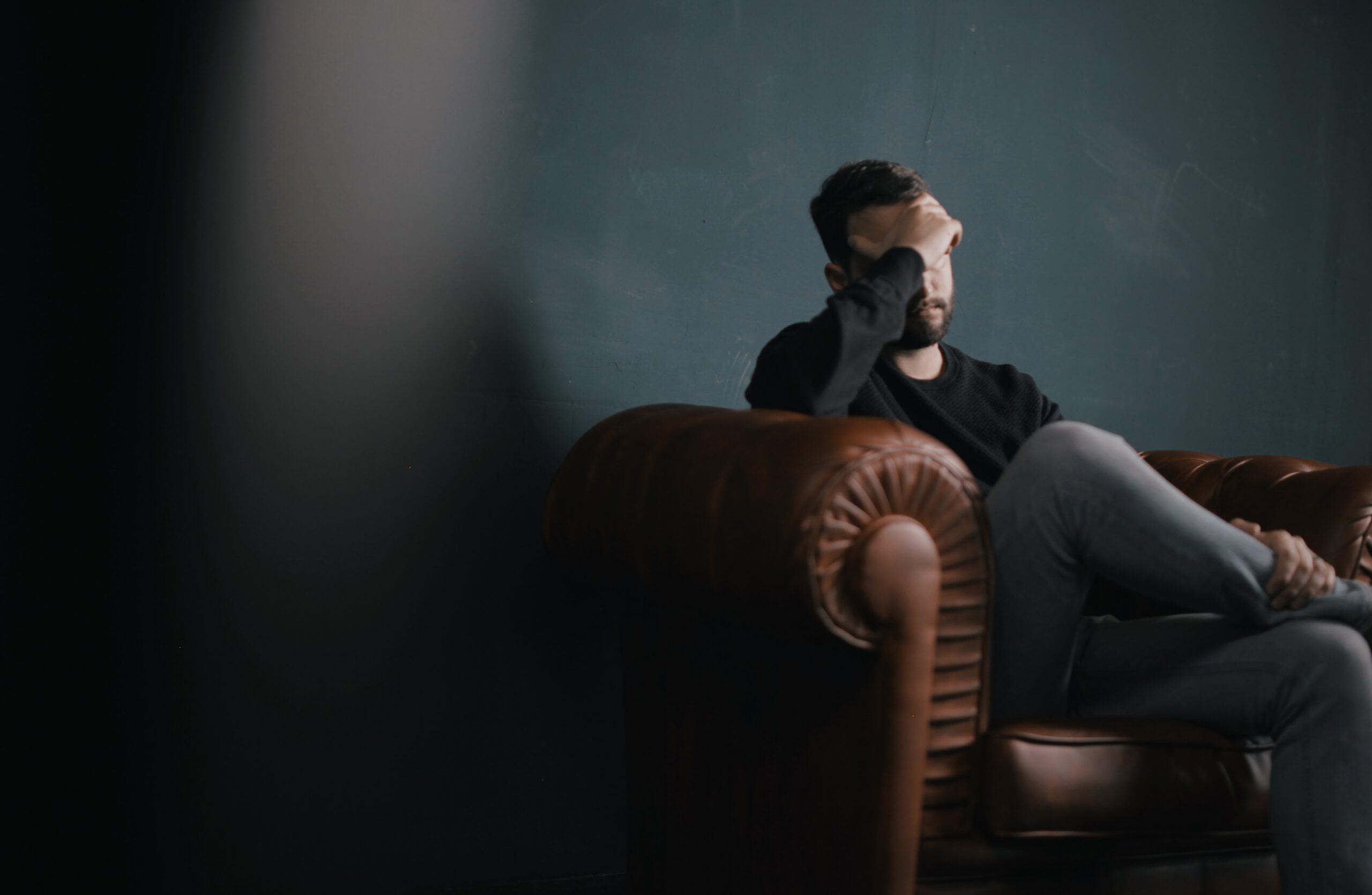 Emotionale Herausforderungen und die Rolle der Traumatherapie Mann sitzt nachdenklich auf einem Sofa und blickt auf den Boden. Traumatherapie bei Heilpraktikerin für Psychotherapie kann Unterstützung bieten.